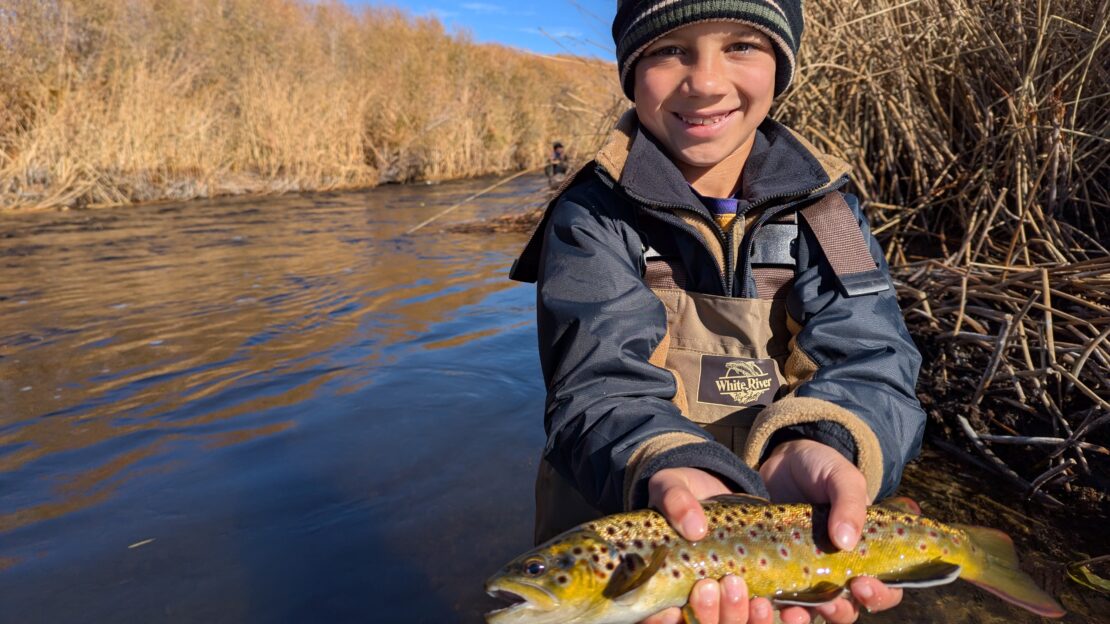 young boy holds up a wild brown trout he caught in the Lower Owens River